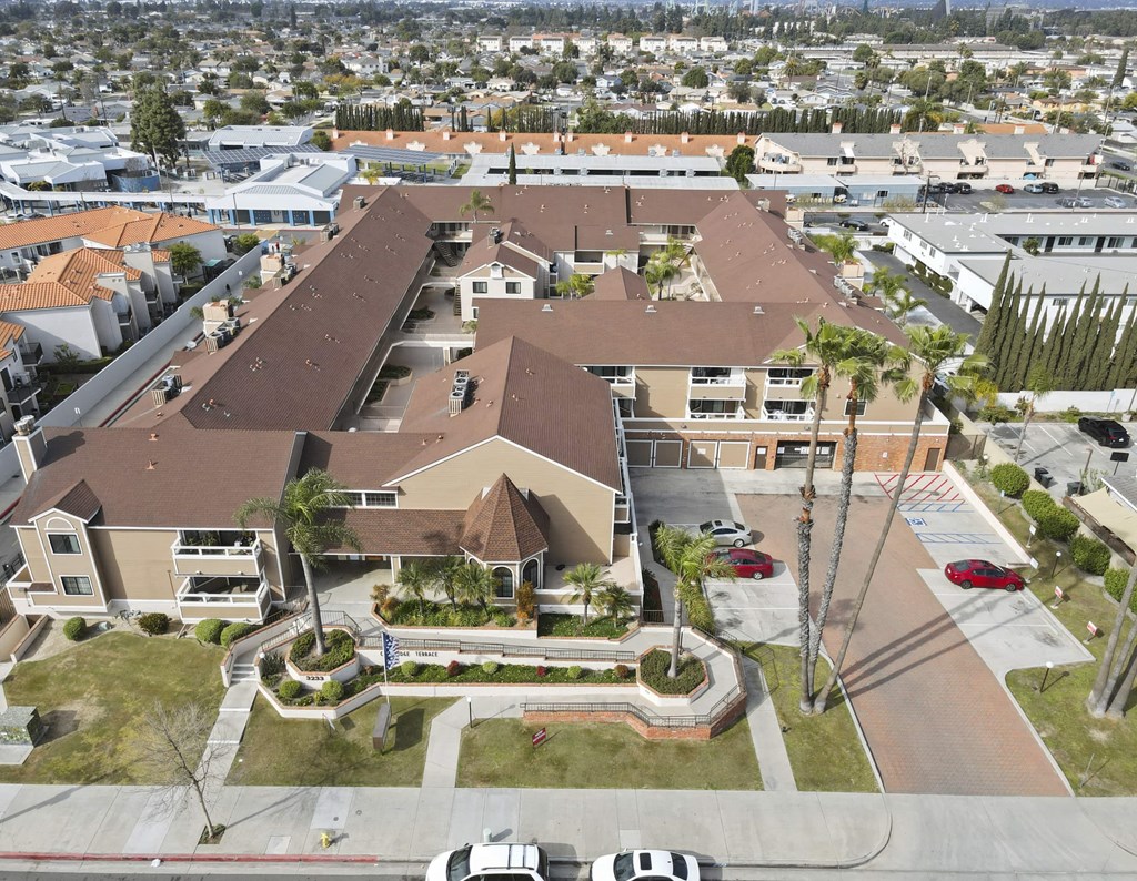 A large building with a brown roof is surrounded by a parking lot and palm trees.