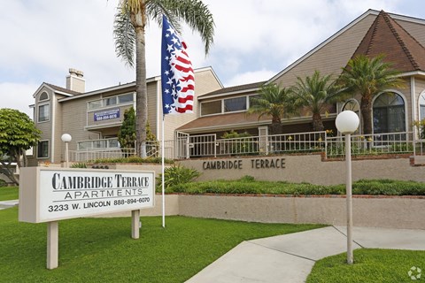 A sign for Cambridge Terrace Apartments is in front of a building with an American flag.