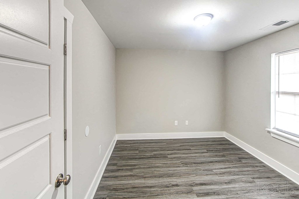 A room with a white door and a window with a grey floor.