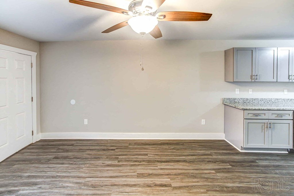 A room with a ceiling fan and a kitchenette.