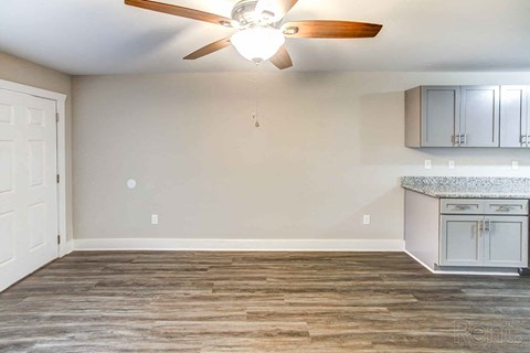 A room with a ceiling fan and a kitchenette.
