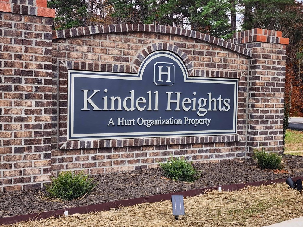 A sign that says "Kindell Heights" is mounted on a brick wall.