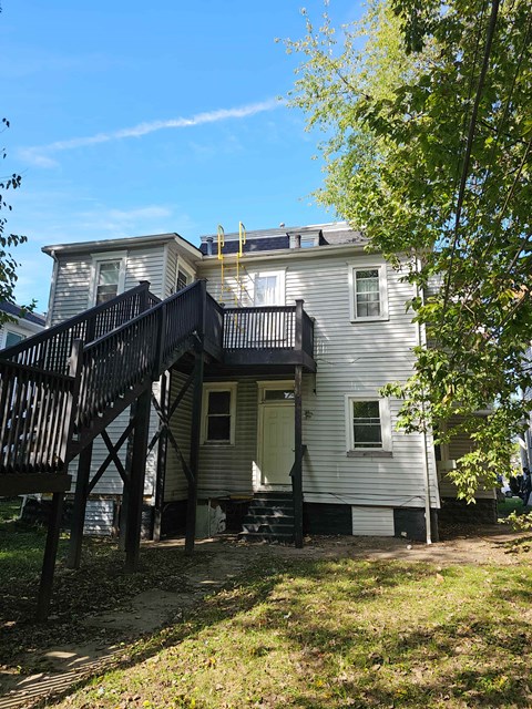 A two-story house with a balcony and a tree in front.