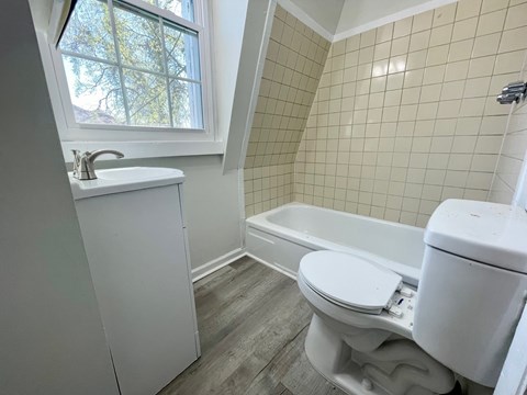 A white toilet sits in a bathroom with a white sink and bathtub.