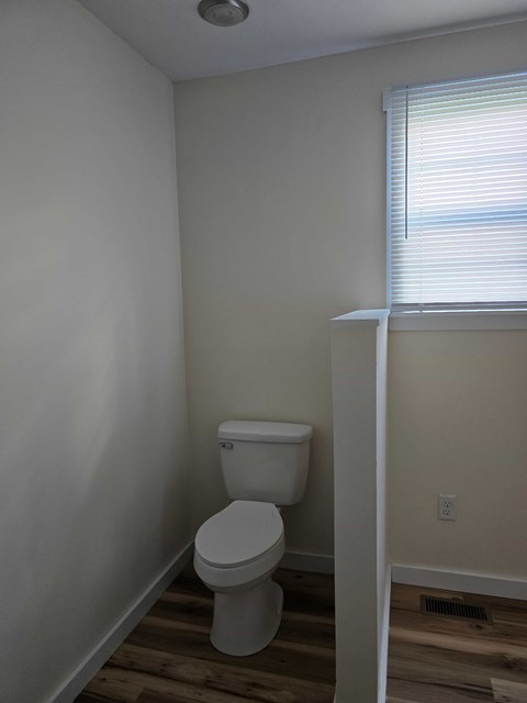 A white toilet in a small bathroom with wood flooring.