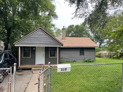 a small gray house with a yard and a fence