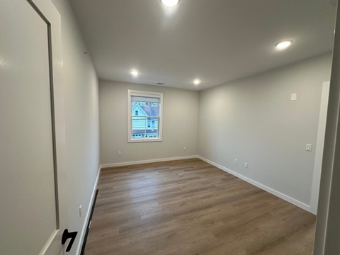 A room with wooden flooring and a window showing a view of a house.