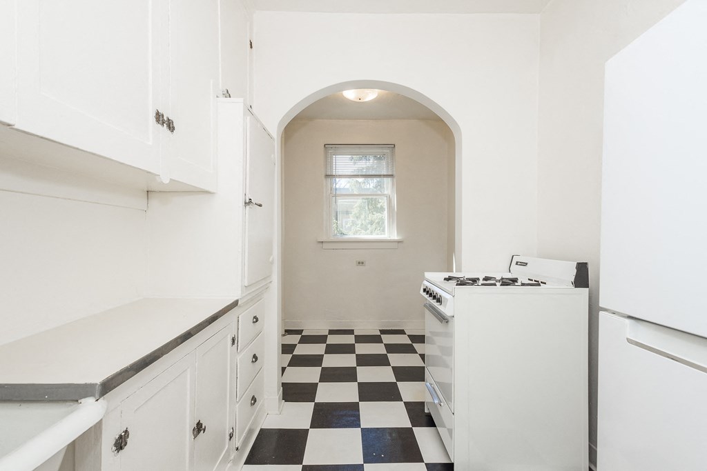 A kitchen with white cabinets and a black and white checkered floor.