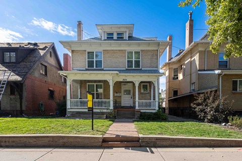 the front of a brick house with a porch and a yellow sign