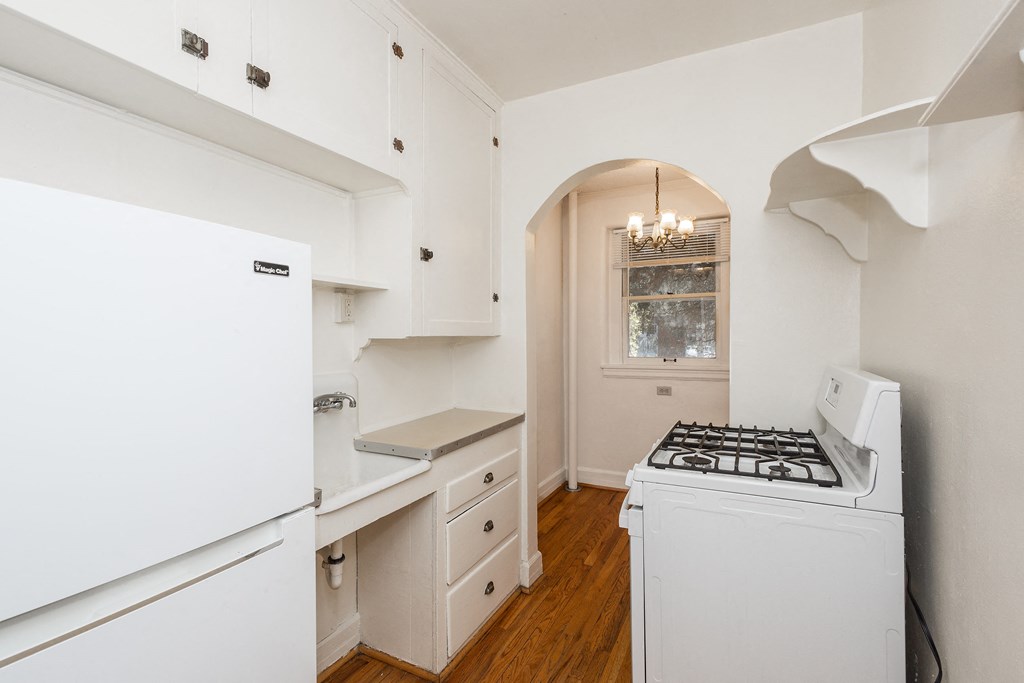 A white fridge in a kitchen with wooden floors and a white stove.