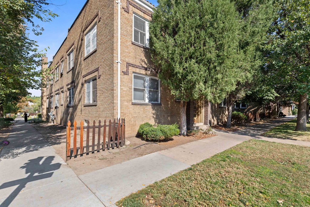 a brick apartment building with a sidewalk and a wooden fence