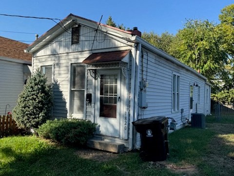 a small white house with a trash can in front of it