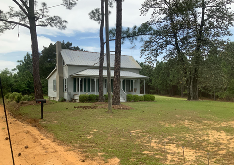 a white house with a dirt road and some trees