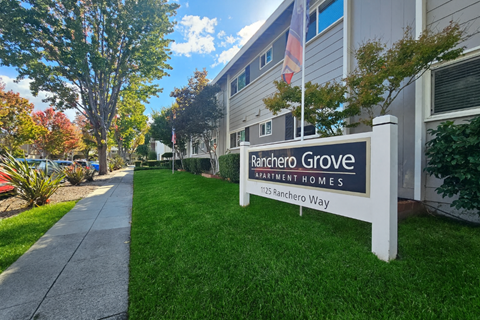 A sign for Rancher Grove Apartment Homes stands in front of a building.