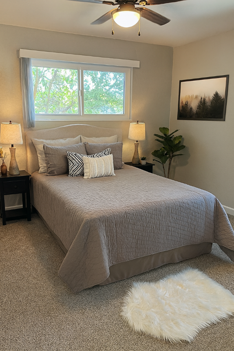 A bedroom with a bed, two lamps, a fan, and a rug.