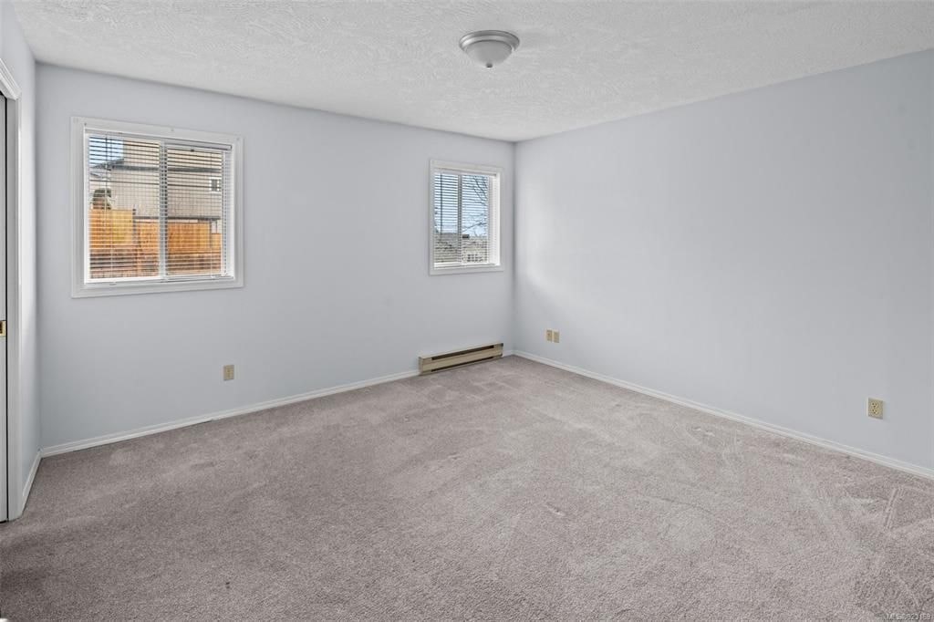A room with a carpeted floor and two windows.