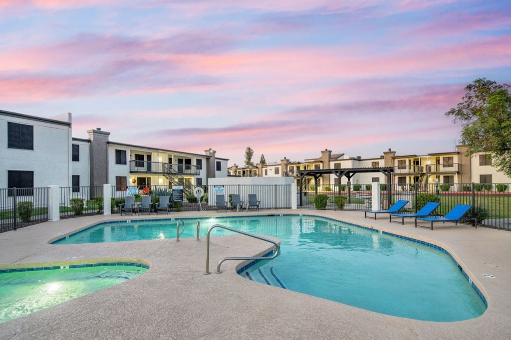 A swimming pool surrounded by lounge chairs and apartment buildings.