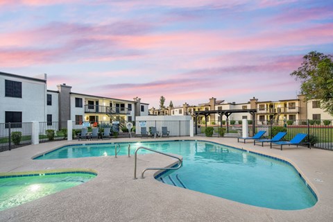 A swimming pool surrounded by lounge chairs and apartment buildings.