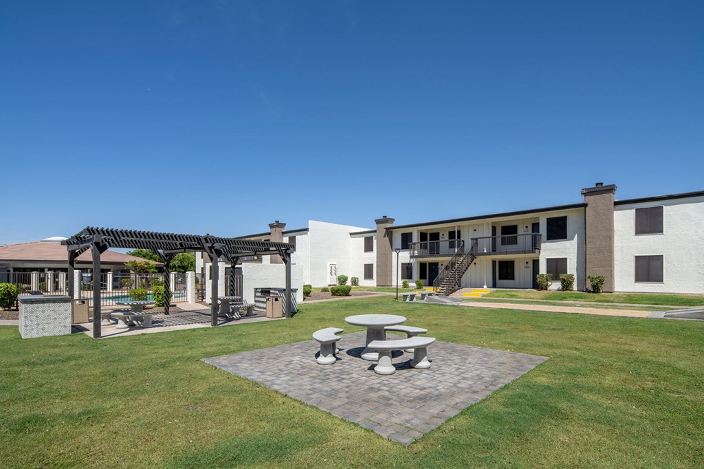 A white building with a pergola and picnic tables in front.