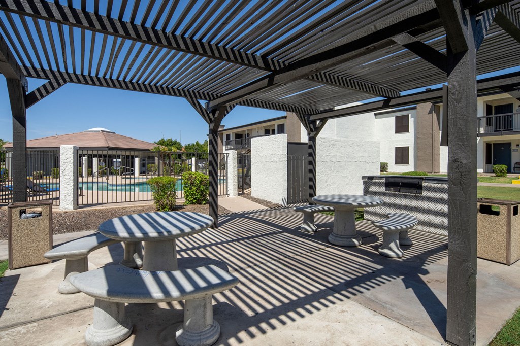 A patio with tables and benches under a striped awning.