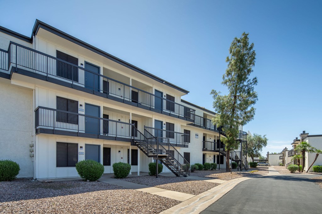 A row of white apartment buildings with black railings and a clear blue sky.