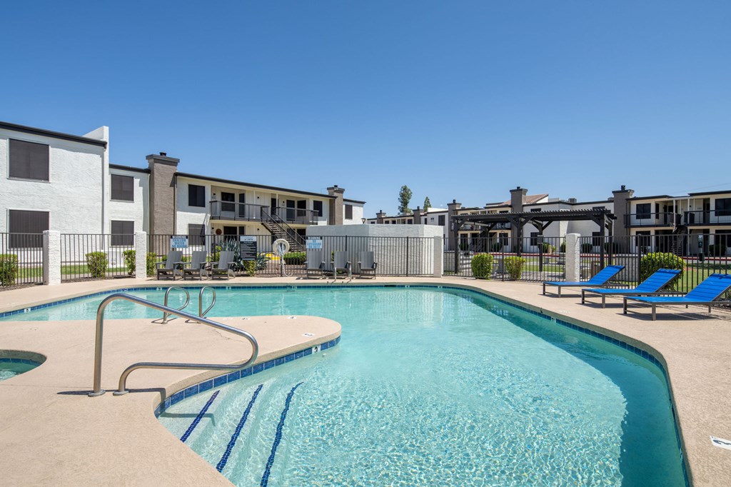 A swimming pool with a slide and sun loungers in front of apartment buildings.