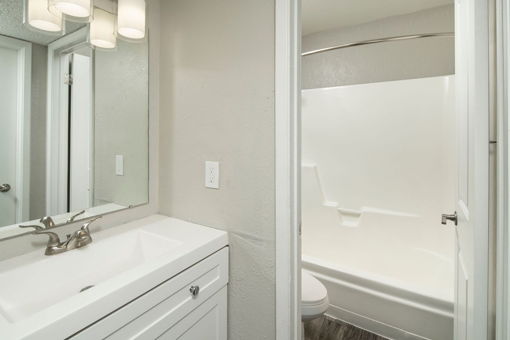 A white bathroom with a sink, mirror, and bathtub.