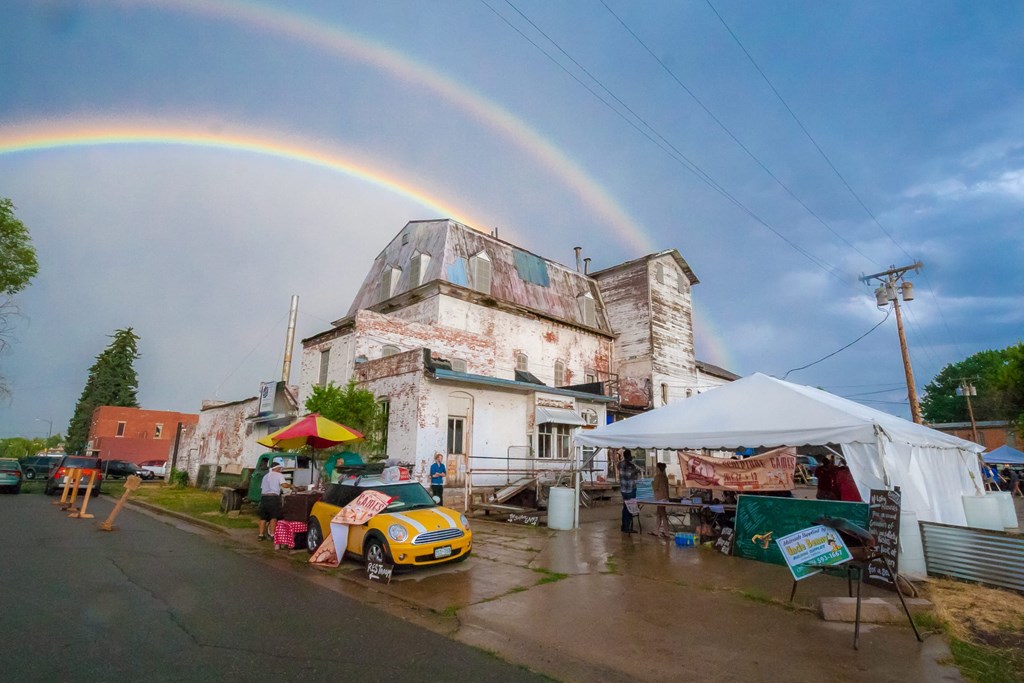 a rainbow in the sky above a small town market with a yellow car