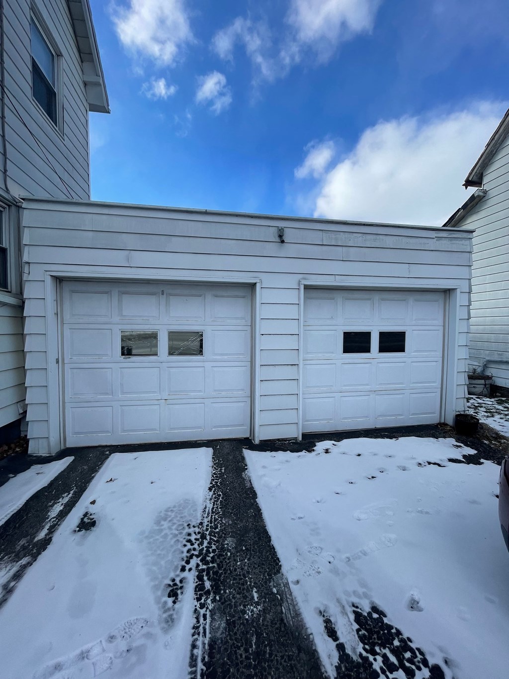 A house with two white garage doors and a snow-covered ground.