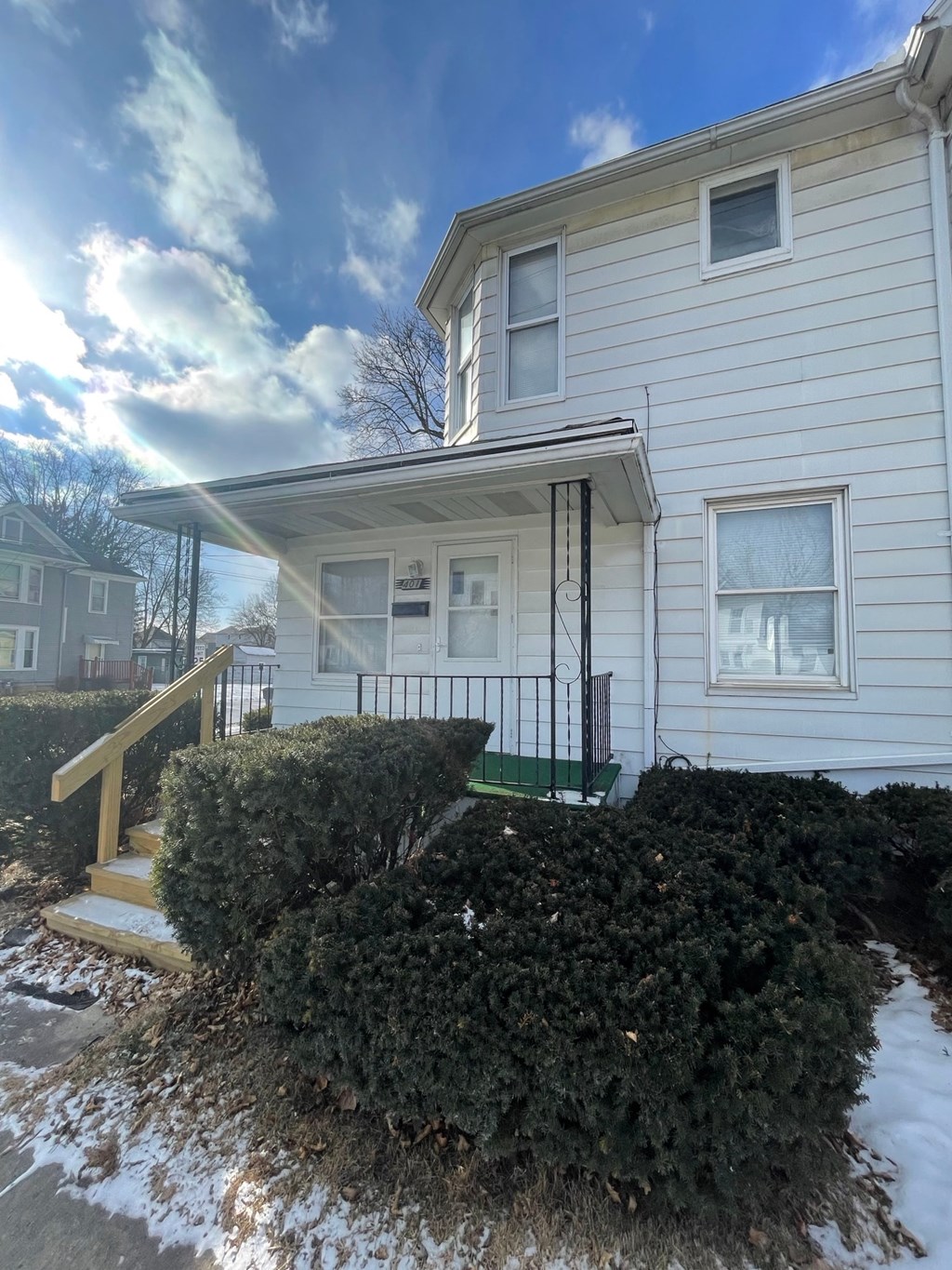 A house with a white siding and a green bush in front.