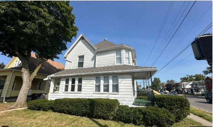 A white house with a grey roof and a tree in front.