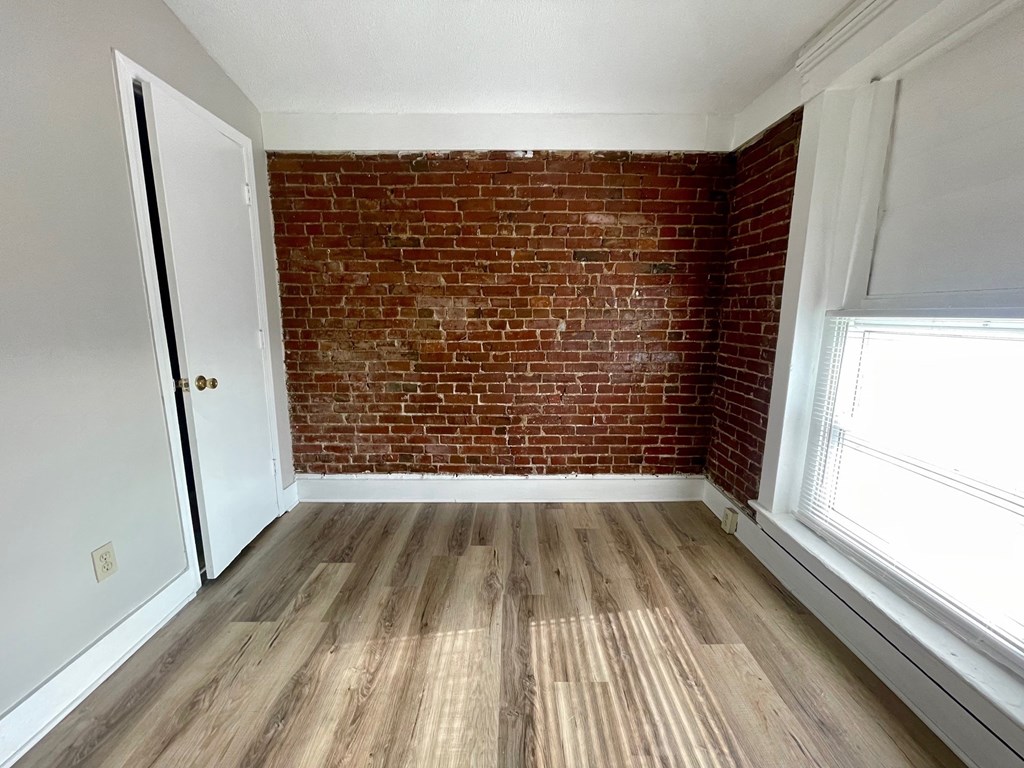 A room with a wooden floor and a red brick wall.