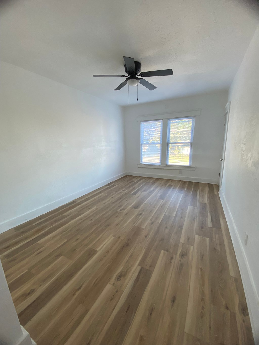 A room with a ceiling fan and wooden flooring.