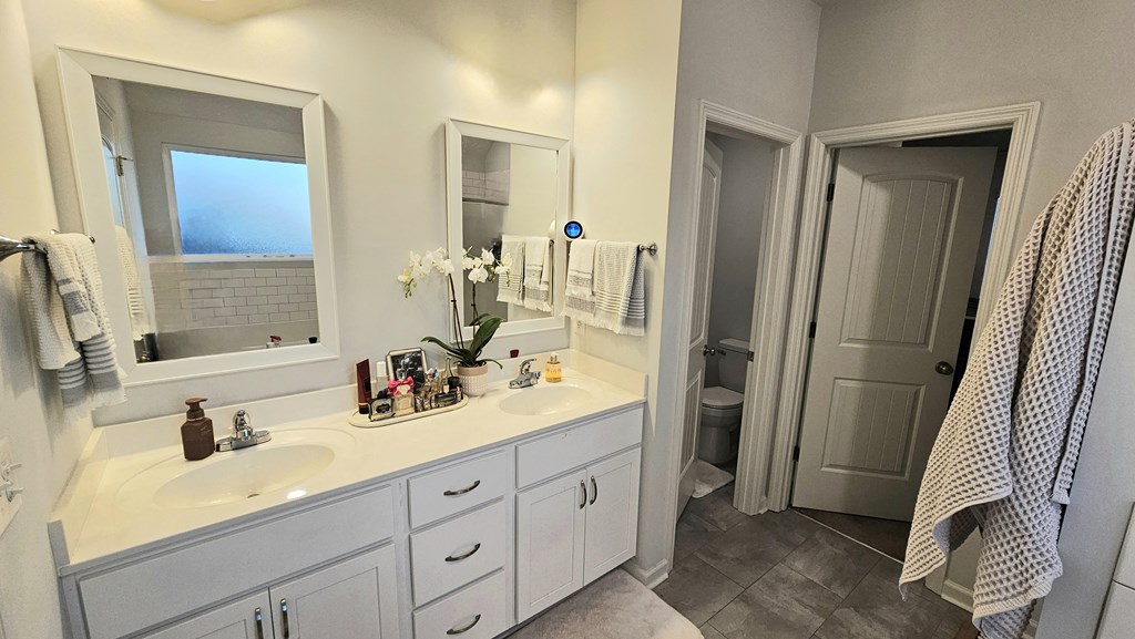 A bathroom with a white counter and a grey towel hanging on the door.