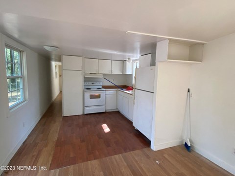 an empty kitchen with white cabinets and a wooden floor