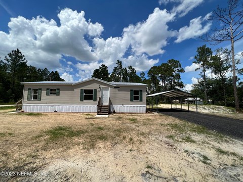 A house with a grey roof and white walls is surrounded by a grassy area with a few trees.