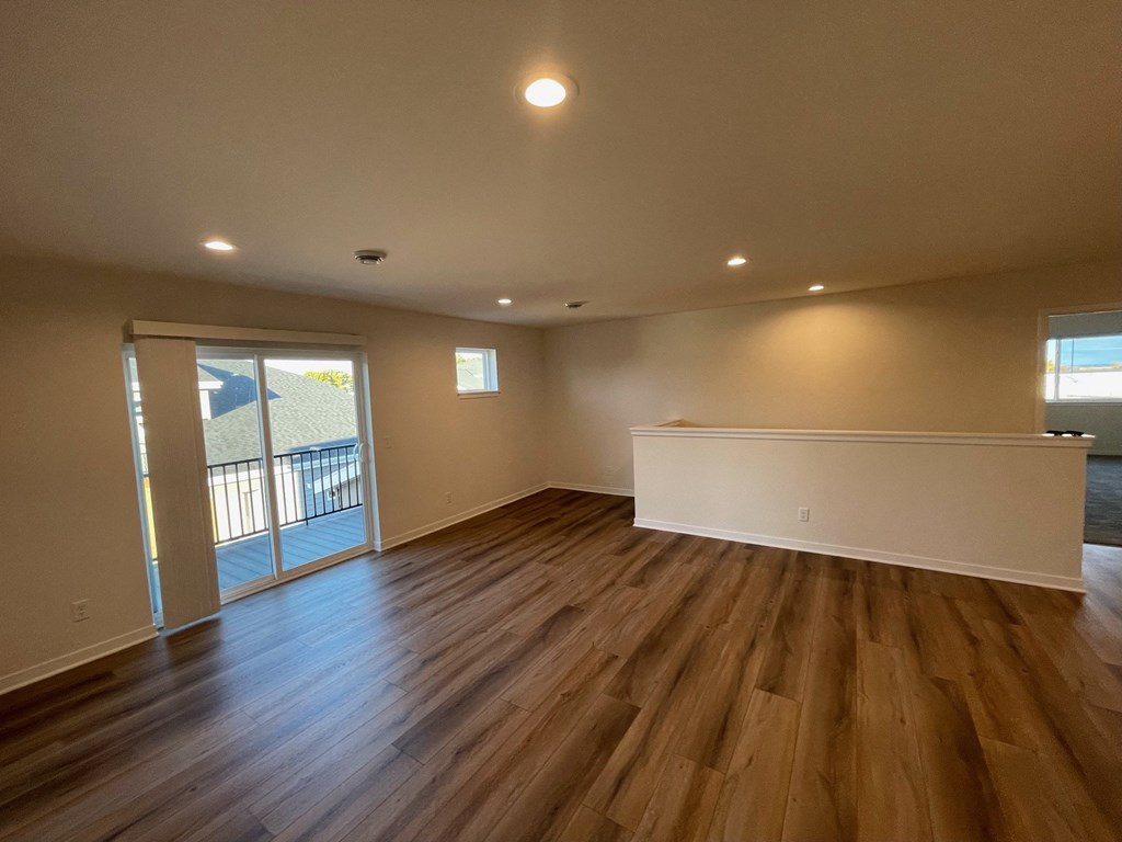 an empty living room with wood flooring and a door to a balcony