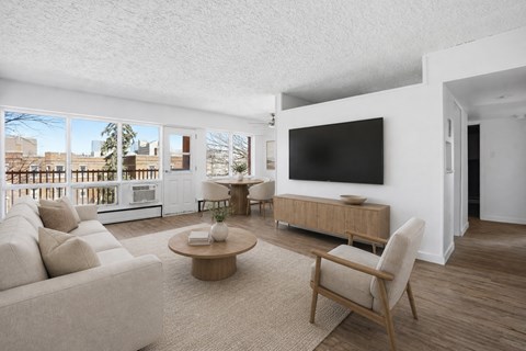 A living room with a white couch, a wooden coffee table, and a large flat-screen TV mounted on the wall.