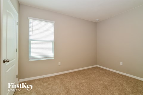 a bedroom with beige carpet and a window and a white door
