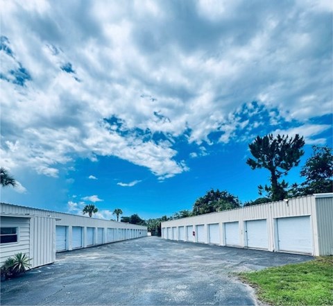 A long row of white garage doors under a blue sky with clouds.