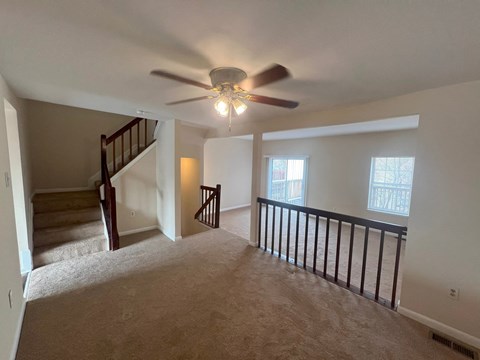 A spacious room with a staircase and a ceiling fan.