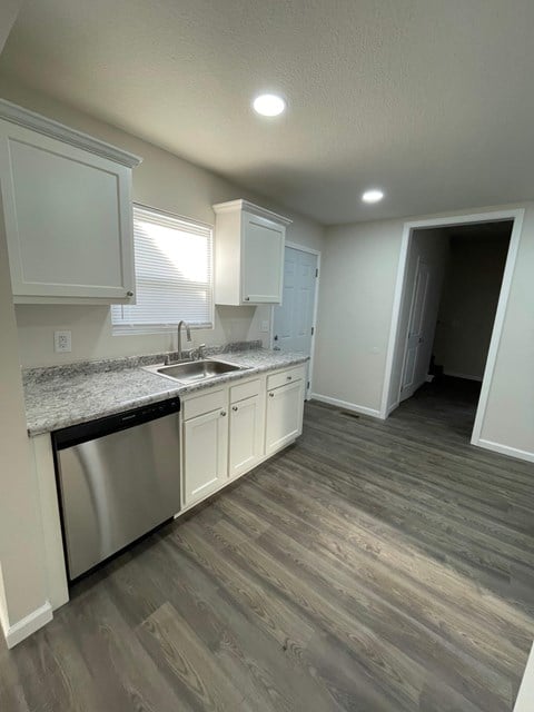 A kitchen with a stainless steel dishwasher and white cabinets.
