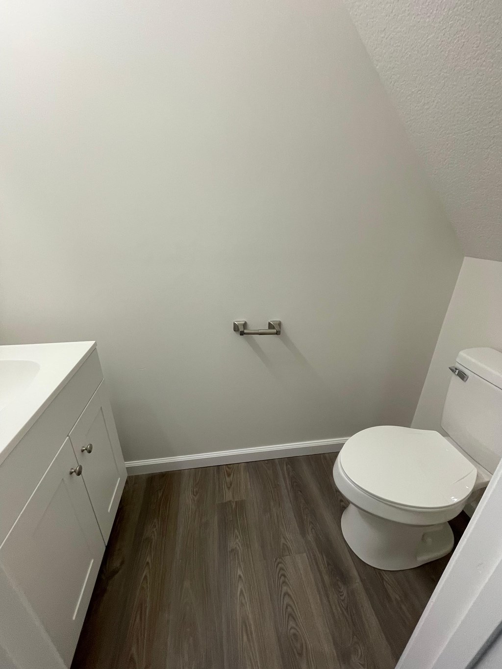 A white toilet sits in a bathroom with a white cabinet and a white sink.