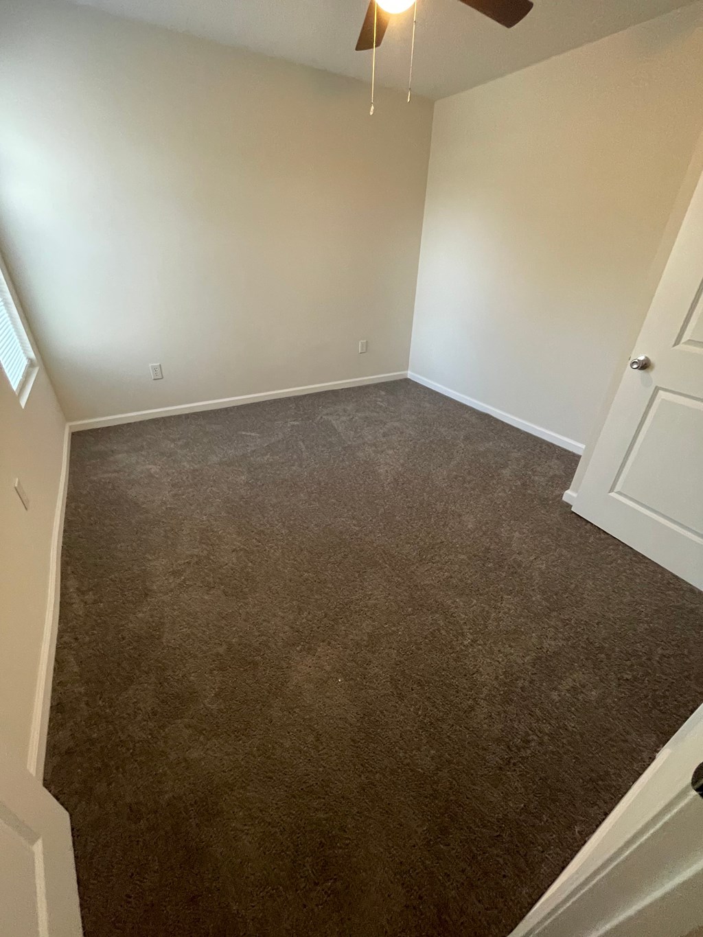 A room with a carpeted floor and a ceiling fan.