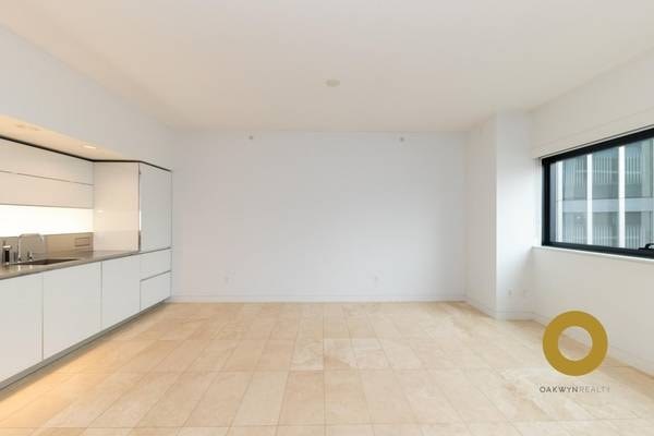 an empty living room with a kitchen and a window
