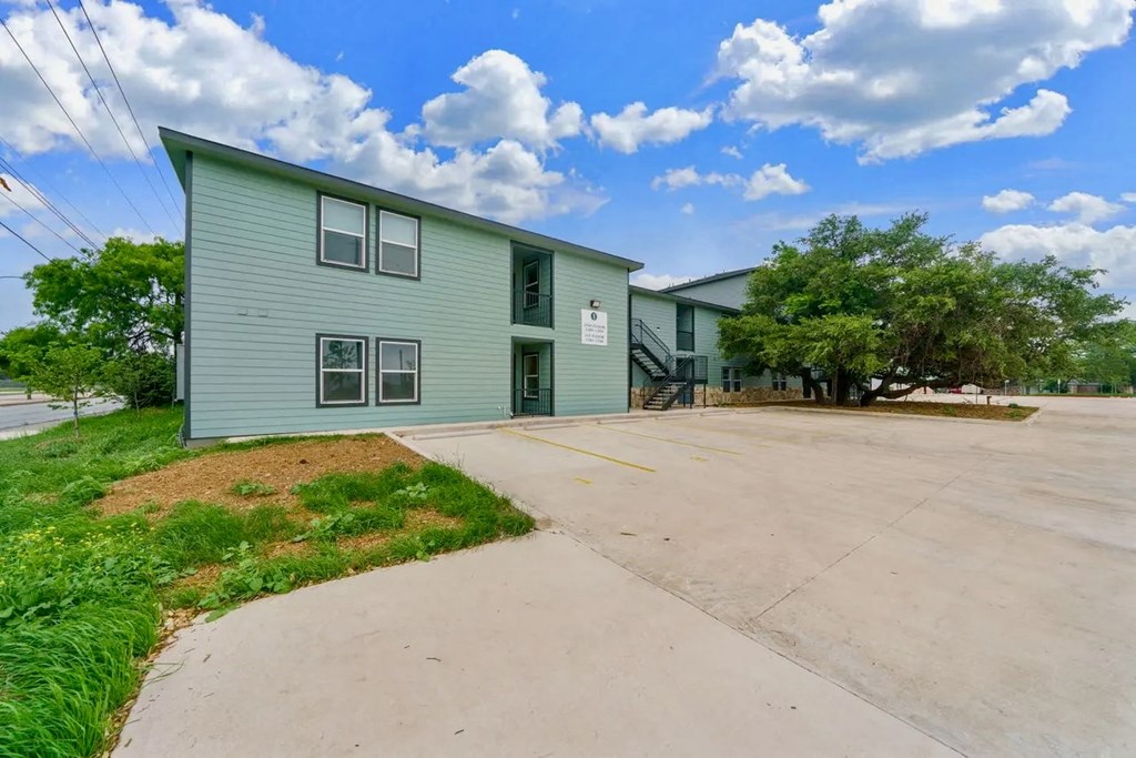 the front of a green building with a driveway and a blue building next to it