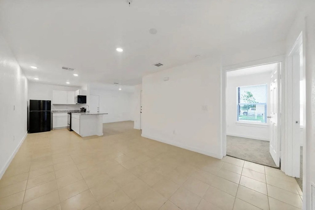 the living room and kitchen of a home with white walls and tiled floors