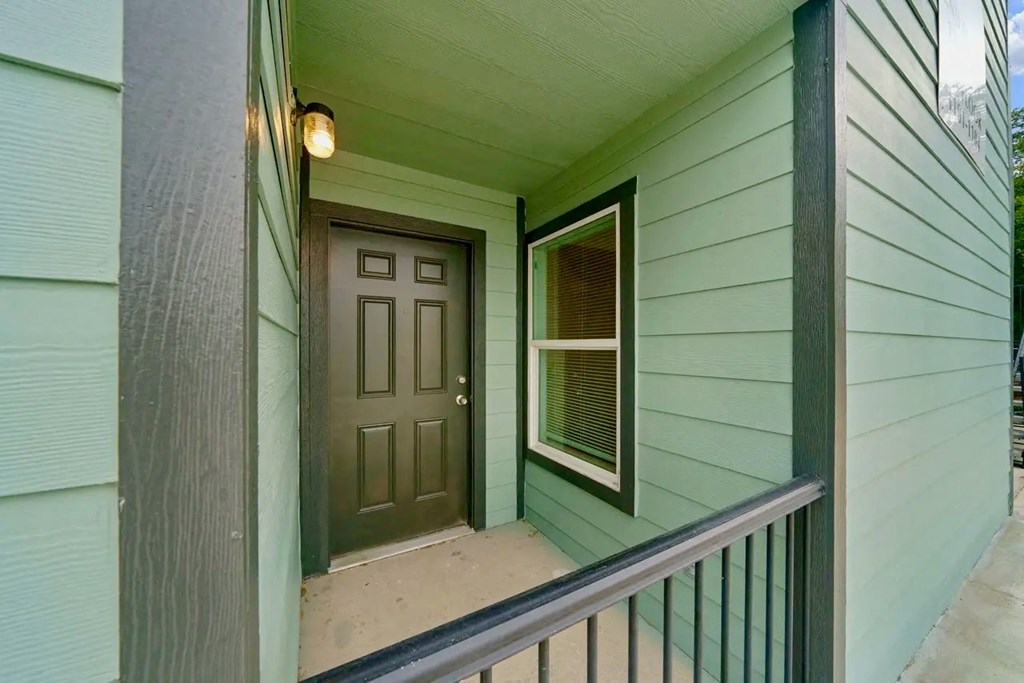 the front door of a green house with a porch