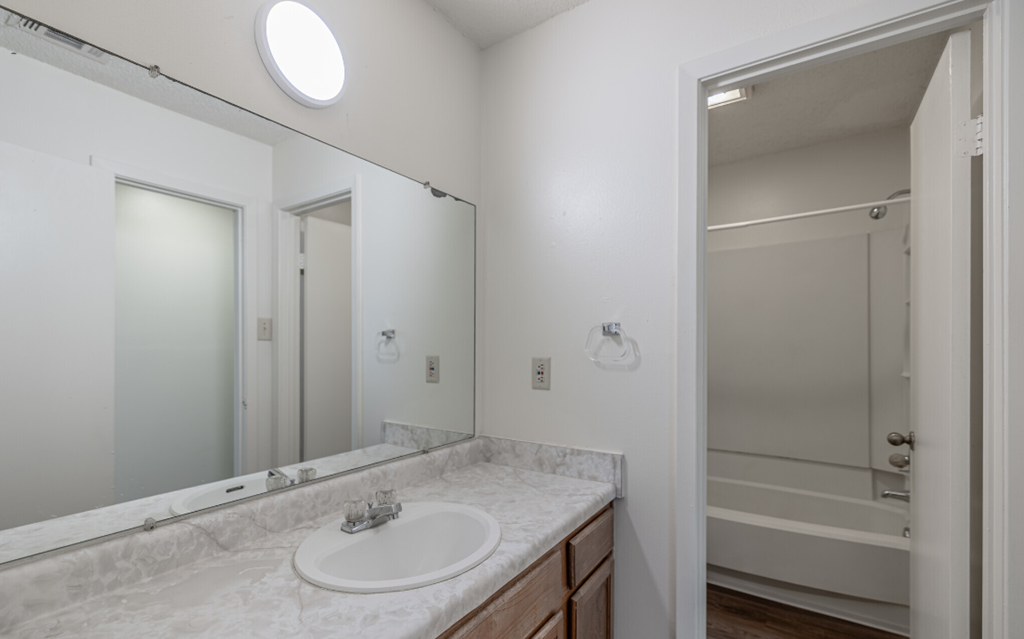 A bathroom with a marble countertop and a round mirror.