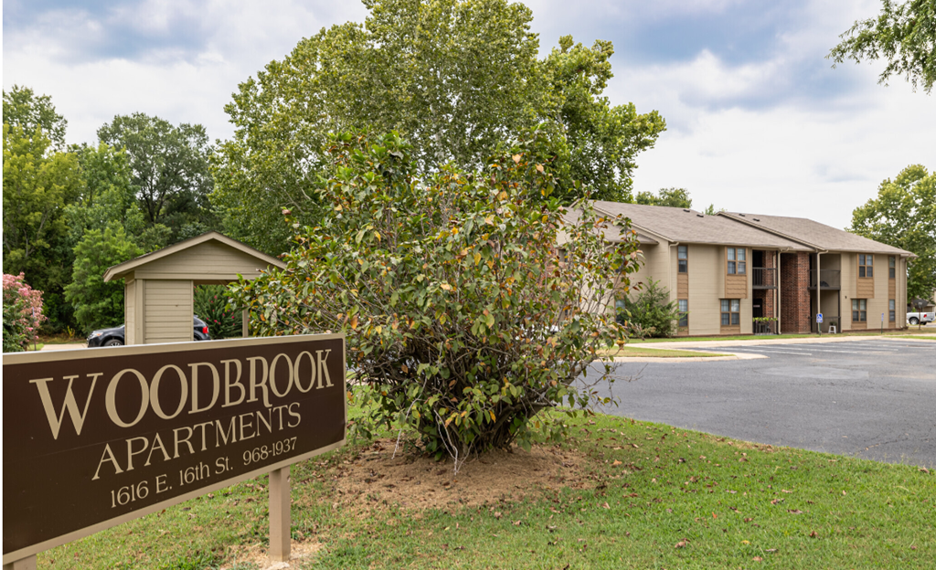 A brown sign that says Woodbrook Apartments in front of a building.